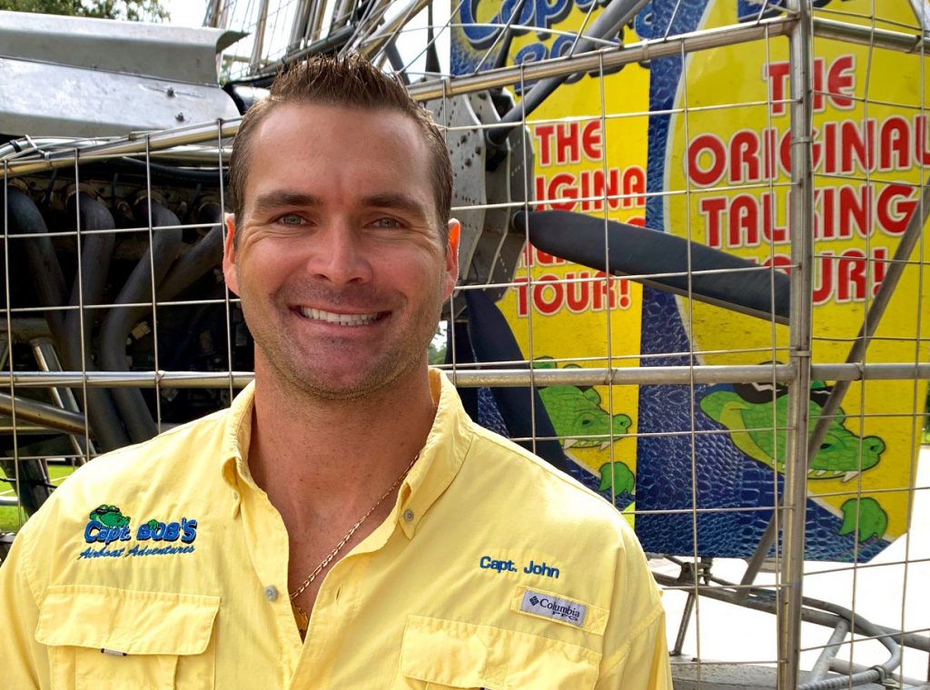 Captain John smiling in front of the Captain Bob's Airboat Adventures tour sign.
